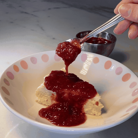 Geleia de morango sendo colocada sobre uma fatia de cheesecake basca